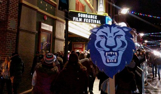Street in Park City, Utah with Sundance Film Festival in the background and someone in a crowd carrying a Columbia Athletics Lion sign in the foreground.
