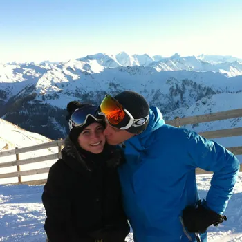 Male and female couple in a ski setting. Male is kissing female on the cheek.