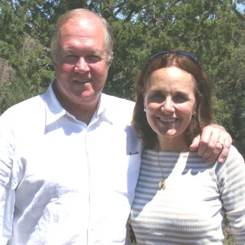Male and female couple with their arms around each other, standing in front of green trees.