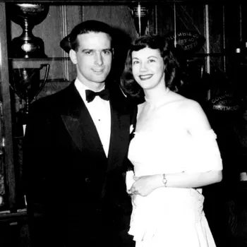 Black and white photo of man on the left and women on the right smiling and side hugging to face the camera.