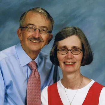 Professional photo of tall man with glasses standing next to a women with a bib.