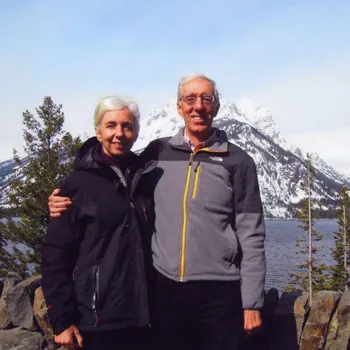 Male and female couple standing in front of a snowy mountain.