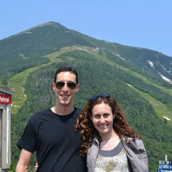Male and female couple standing in front of a hilly landscape.