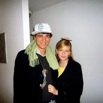 Young man with $ hat on and young women affectionately holding is arm.