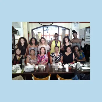 Group of women in a dining hall, one row sitting and a row standing behind.