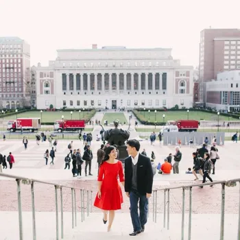 Female in red dress and male on black business casual walking up Low Library steps with Butler Library in the backgroud.