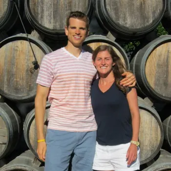 Male and female embracing on a sunny day with horizontally stacked kegs in background.
