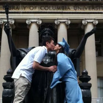 Young couple kissing in front of Alma Mater statue with the women in Columbia university alum robes.