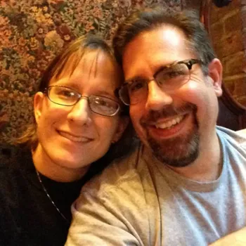 Smiling couple both wearing glasses with a floral background.