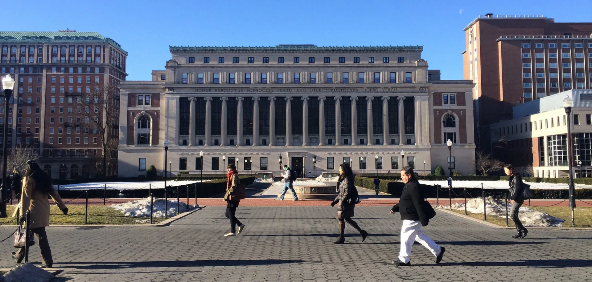 Butler Library at Columbia University with people walking across the campus plaza on a clear day.