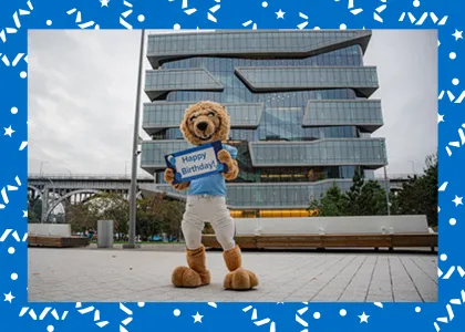 Roar-ee in front of the Kravis building, holding a "Happy Birthday" sign
