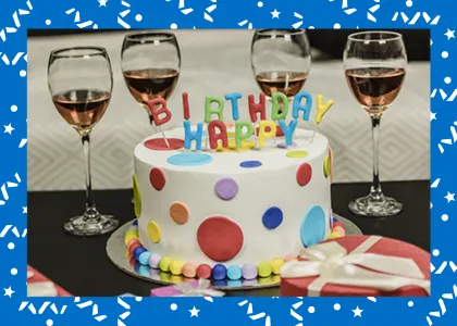 Colorful birthday cake surrounded by four half-filled wine glasses.
