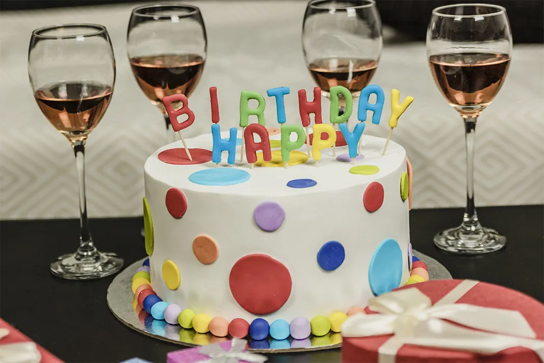 Colorful birthday cake and half-full wine glasses containing rose.