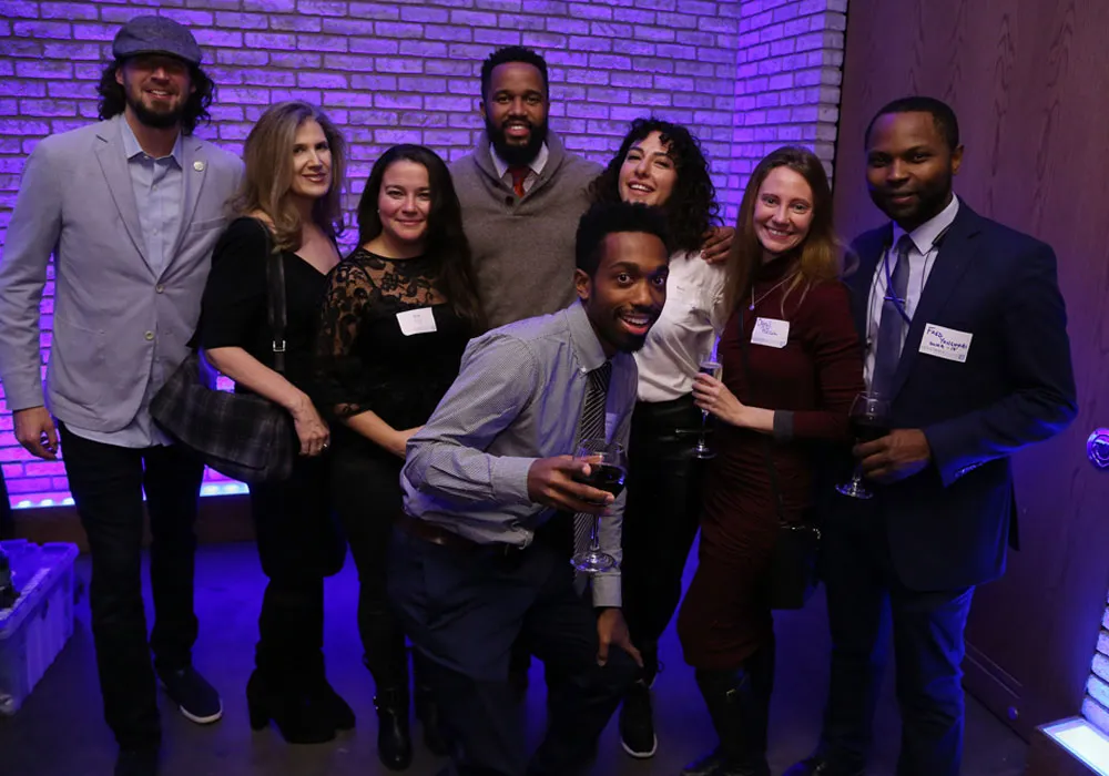 A diverse group of alumni at an event, looking at the camera. Some hold wine glasses.