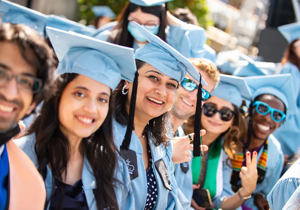 Columbia students in caps and gowns at the graduation ceremony, smiling at the camera.