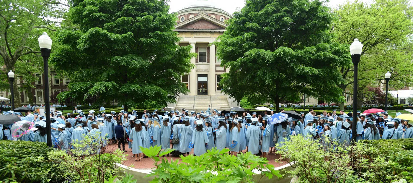 Graduates in caps and gowns gathered on Columbia University campus lawn.