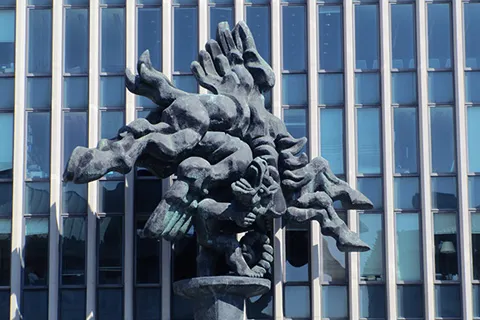 Abstract sculpture of intertwined human figures in front of a modern glass building (Columbia Law School).