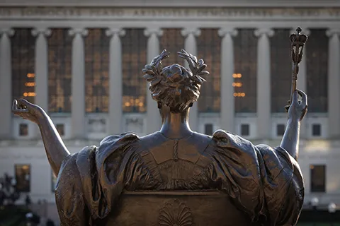 Bronze statue with raised arms facing a large columned university building (Low library.)