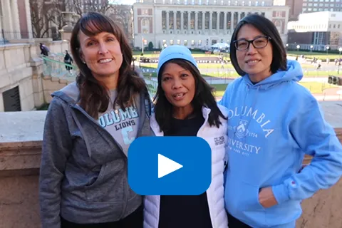 Three people standing together on a university campus, with a play button overlay.