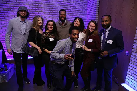 Group of people posing together at an indoor event with purple lighting.