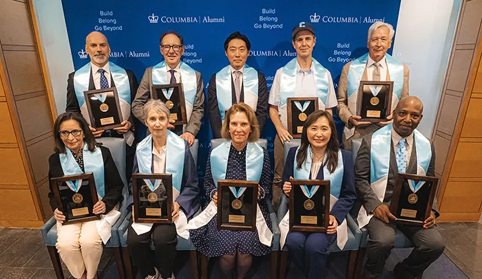 All 10 alumni medalists, in front of the Columbia Alumni banner and holding their alumni medal.