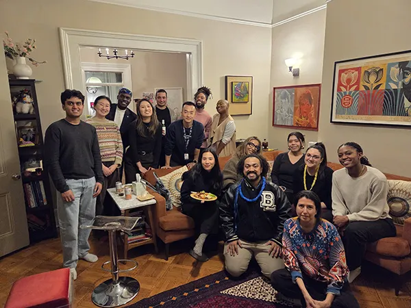 Group of students and alumni sitting in a living room at a casual  gathering.