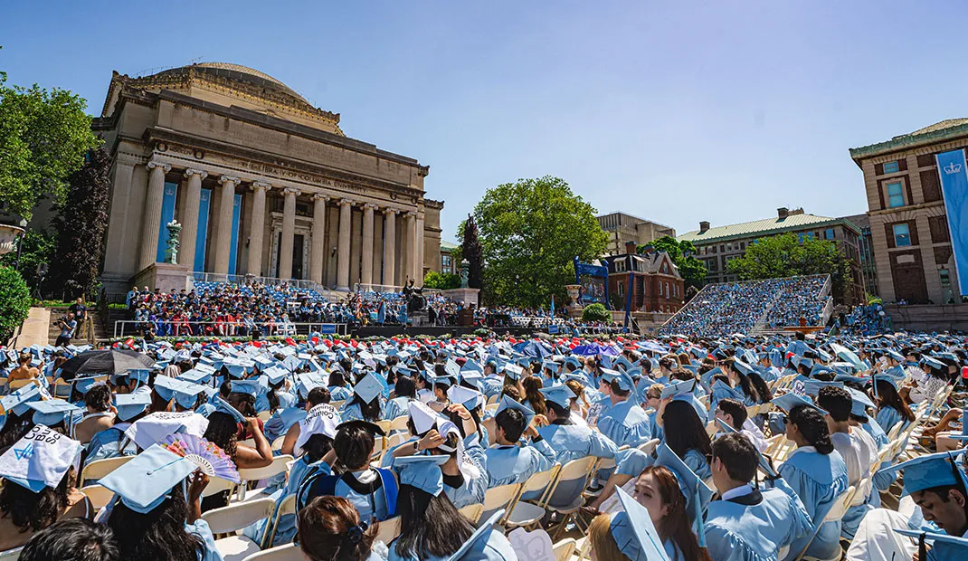 View of Low Library during commencement with graduating students in blue regalia.