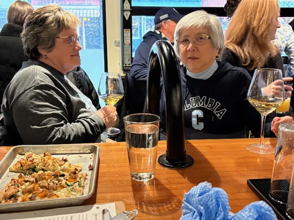People sitting at a bar with drinks and food, talking in a casual indoor setting.