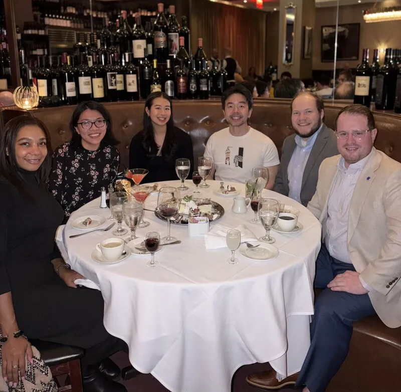 Alumni and students sitting at a round table in a restaurant and smiling.