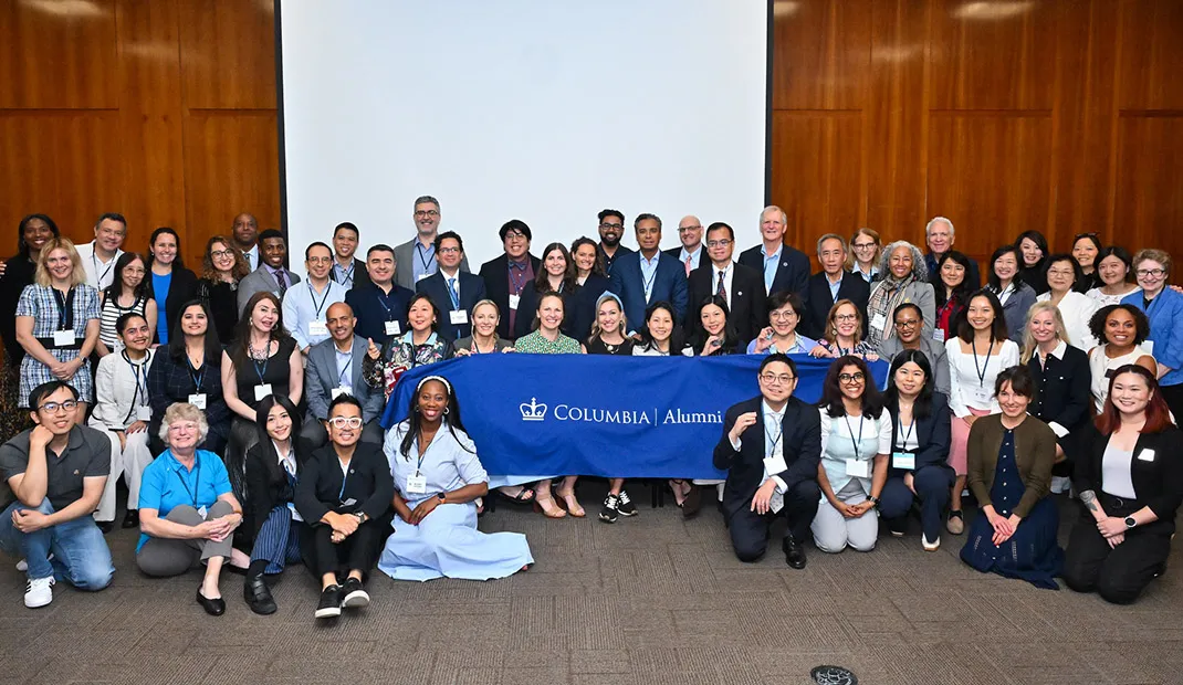 Large group of alumni posing together at the Leaders Experience conference, holding a Columbia Alumni banner.