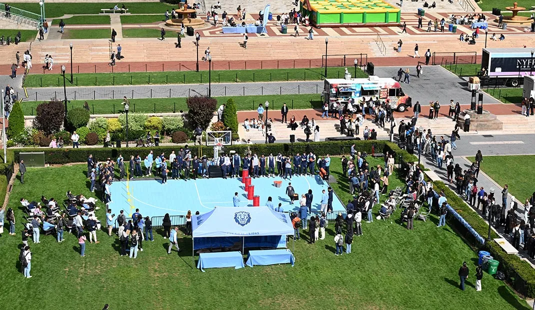 Students gathered around an outdoor basketball court event on campus, with tents and spectators nearby.
