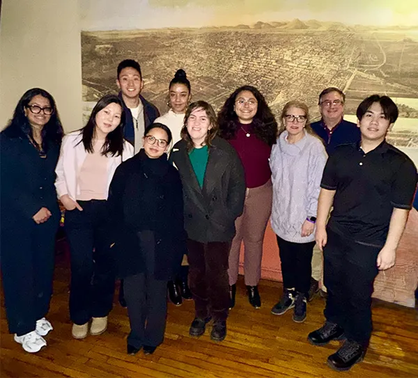 Alumni and students posing together in front of a photograph.